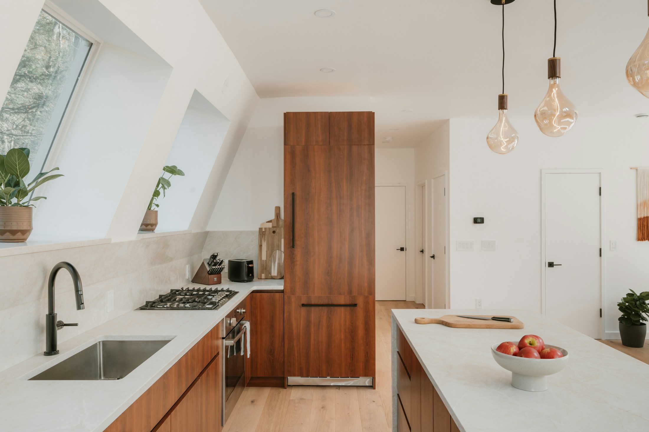 Architectural kitchen with warm timber cabinetry, pale stone worktops and natural light from angled windows